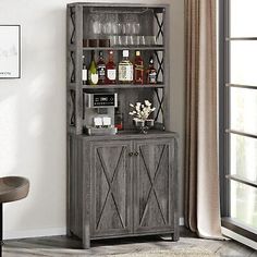 a tall wooden cabinet sitting next to a window filled with bottles and glasses on top of it