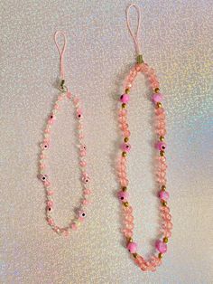 two bracelets with pink beads and gold accents on a white tablecloth, one is hanging from a hook