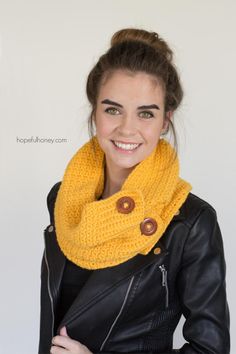 a woman wearing a yellow scarf and black leather jacket smiles at the camera while standing in front of a white wall