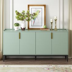 a sideboard with plants and candles on it in front of a framed painting above