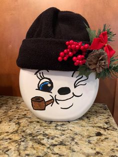 a white bowl with a black hat and red berries on it sitting on a counter