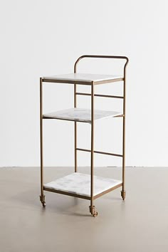 a gold and marble serving cart with two shelves on each side, against a white wall