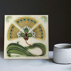 a white vase sitting on top of a table next to a ceramic wall plaque with a peacock design