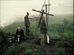 three men sitting on the ground in front of a cross