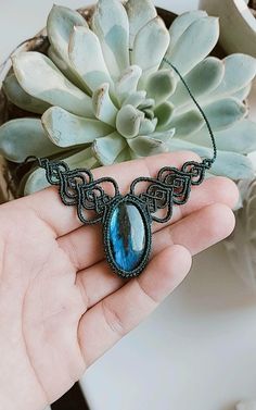 a hand holding a blue stone pendant next to a succulent plant