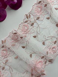 pink and gold embroidered fabric with flowers on white tablecloth next to purple orchids