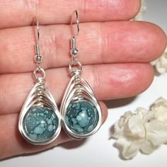 a pair of silver and turquoise earrings on a person's hand with flowers in the background