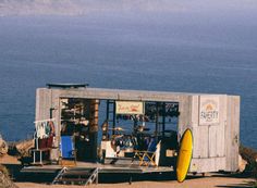 an outhouse on the beach with a yellow surfboard