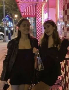 two beautiful women standing next to each other in front of a red and white checkered wall