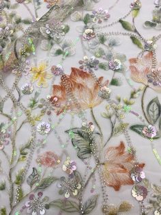 an embroidered fabric with flowers and leaves on it's side, in pastel colors