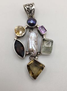 Beautiful designed - multi shapes and 7 gemstones on the 925 silver holder Pendant with round clasp. The pendant mix of Amethyst, Green Quartz, Citrine and Smoky Quartz, Mother of Pearl. Good pre-own condition. It stamped "925" on the silver holder.  Pendant Size: 2 3/4" (H) x 1 3/8" (W) (6 cm x 3.5 cm) with the top clasp. Weight:  23 grams (0.7 Troy Ozs)  Item is exactly as shown in pictures.   Please carefully review the item description and accompanying pictures before making a purchase, as w Sterling Silver Gemstones With Natural Stones For Anniversary, Sterling Silver Multi-stone Round Pendant Jewelry, Sterling Silver Multi-stone Round Pendant, Fusion Style Sterling Silver Gemstones, Anniversary Sterling Silver Gemstones With Natural Stones, Multi-stone Pendant Gemstones For Jewelry Making, Round Multi-stone Gemstones In Sterling Silver, Silver Gemstones With Accents As A Gift, Round Multi-stone Sterling Silver Gemstones