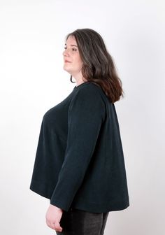 a woman standing in front of a white wall wearing a black sweater and jeans, with her back turned to the camera