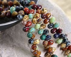 multicolored glass beads are sitting on the ground next to a metal bowl full of them