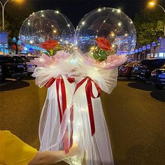 two clear bubbles with red bows and roses in them are on display at an outdoor event