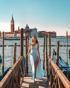 a woman in a blue dress is standing on a pier near the water and buildings