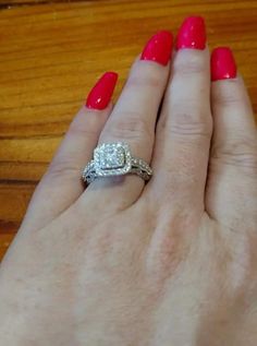 a woman's hand with red nail polish holding a diamond ring