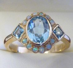 This STUNNING Vintage Inspired ring has been majestically crafted from 9ct Solid Yellow Gold. A bezel set HUGE Oval cut NATURAL Topaz brings this ring to life along with two Vibrant Square cut NATURAL Topaz resting on the shoulders adding additional appeal to this exquisitely feminine ring. Surrounding the face of this GORGEOUS ring are accentuating GENUINE Australian Opals which have been magnificently inset adding fire and exotic appeal to any lady who appreciates wearing such a fine ring ! TH Fire Topaz Ring, Blue Board, Vintage Inspired Rings, Fine Ring, Sparkly Things, Square Cut, Opal Ring, Multi Stone Ring, Jewellery Designs