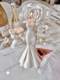 a woman holding a candle in her hand next to some wine bottles and candlesticks