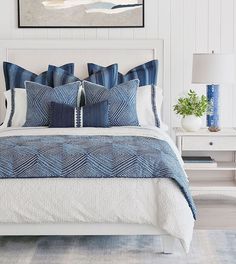 a bed with blue and white pillows on top of it next to a night stand