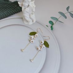 a pair of earrings with flowers and leaves are on a plate next to a figurine