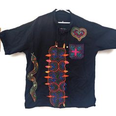 Peruvian Unisex T-Shirt, Meticulously Hand-Embroidered Amidst The Lush Jungle Canopy. Each Stitch Tells A Story Of Ancient Traditions And Vibrant Culture, Making Each Piece A Unique Work Of Art. Adorned With A Charming Pocket On The Right Side And A Captivating Heart-Shaped Snake Motif, This Shirt Perfectly Combines Style With Sustainability, Made With Love And Care By Skilled Artisans. This T-Shirt Is Handmade By Peruvian Amazon Jungle Artisans. Measure Length 30 Broad 24 Shoulder 18 Embroidered Short Sleeve Shirt With Relaxed Fit, Black Long Sleeve Embroidered T-shirt, Traditional Black Cotton Shirt, Black Embroidered Crew Neck Top, Casual Black Shirt With Floral Embroidery, Short Sleeve Cotton Tops With Embroidery, Black Embroidered T-shirt For Summer, Embroidered Cotton Tops With Short Sleeve, Black Embroidered Cotton Shirt