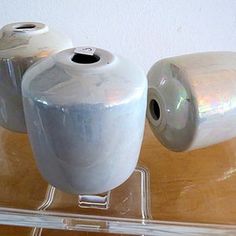 three white vases sitting on top of a clear shelf next to each other and two rolls of toilet paper