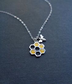 a silver and yellow necklace on a black surface with a bee sitting on top of it