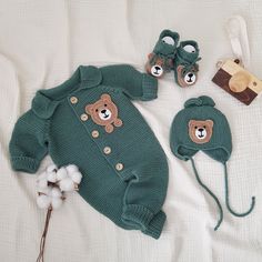 a teddy bear sweater, hat and booties laying on a bed with white sheets