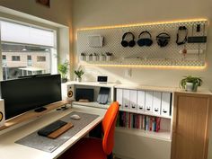 a desk with a computer monitor, keyboard and headphones on it in front of a window