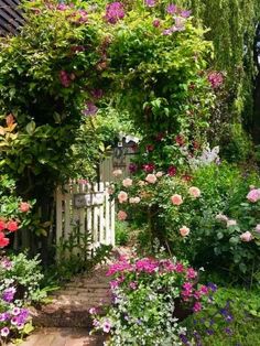 the garden is full of colorful flowers and greenery, with a white gate in the middle