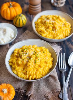 two bowls filled with macaroni and cheese on top of a table next to silverware