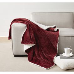 a couch with a blanket on top of it next to a cup and saucer