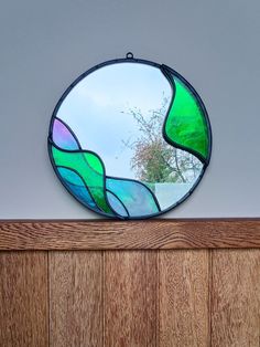 a round stained glass mirror sitting on top of a wooden shelf