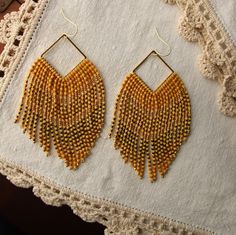 These maxi fringe earrings include three beautiful tones of premium Japanese Miyuki glass beads combined with small gold round beads to create an elegant V pattern. The beads are hand strung and hang from a gold filled square finding.  The have fantastic movement and just the right the amount of sparkle. The square finding is hung from a hypoallergenic 14K gold plated ear wire. These earrings are designed by myself and made in conjunction with my team of women artisans from vulnerable communitie Gold Bohemian Beaded Earrings With Faceted Beads, Bohemian Gold Earrings With Faceted Beads, Bohemian Gold Rectangular Beaded Earrings, Gold Chandelier Earrings With Gold Beads, Elegant Gold Beaded Earrings With Fringe, Elegant Yellow Fringe Earrings, Gold Beaded Fringe Dangle Earrings, Gold Tassel Earrings With Round Beads, Elegant Gold Tassel Earrings With Round Beads