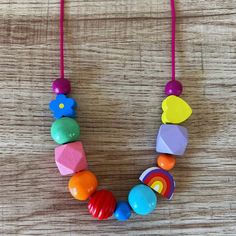 a necklace made out of wooden beads and colorful magnets on a wood table with a pink cord