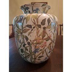 a vase with flowers and birds painted on the front is sitting on a wooden table