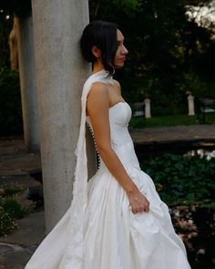 a woman in a wedding dress leaning against a pillar