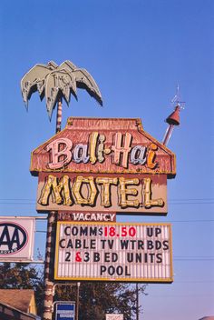 a hotel sign with palm trees on top and other signs in the sky above it