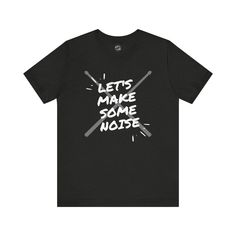 A graphic T-shirt featuring a design of drumsticks and the phrase 'Let's Make Some Noise'. This T-shirt is perfect for music lovers, drummers, and anyone who loves to stand out with a unique style. It gives off a cool, edgy vibe and is great for casual wear or music events. Perfect for birthdays, music concerts, and everyday wear. The available colors are listed in the dropdown menu. You can refer to the color chart to see those colors. Not all colors on the color chart are available for each de Music-themed Slogan Crew Neck Top, Music-themed Slogan Tops With Crew Neck, Music-themed Slogan Top With Crew Neck, Graphic Tee With Slogan For Concert, Band Merch Slogan Top For Fans, Band Merch Top With Slogan For Fans, Music-themed Slogan Tops For Concerts, Music-themed Text Print Crew Neck T-shirt, Music-themed Graphic Tops For Fan Merchandise