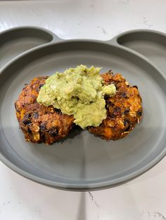 two chicken patties with guacamole on a gray plate in front of some muffins