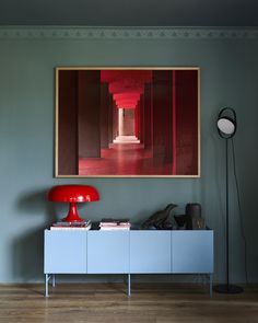 a painting hanging on the wall next to a blue cabinet with a red lamp in it