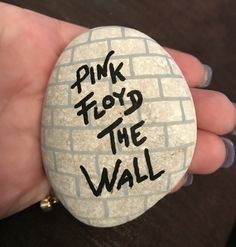 a hand holding a rock with the words pink floyd the wall written on it in black ink