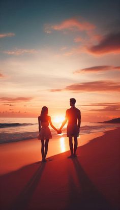 two people holding hands while standing on the beach at sunset or sunrise with their arms around each other