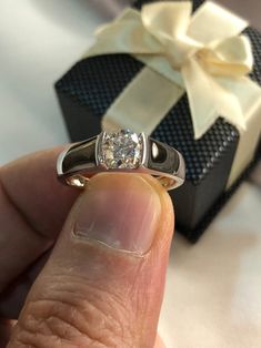 a person holding a ring in their hand with a gift box behind them on the table