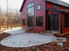 a red house with black windows and brick walkway leading up to the front door is surrounded by autumn leaves