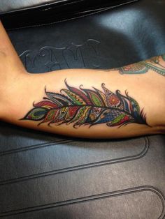 a person with a tattoo on their arm that has a colorful feather design on it