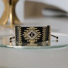 a close up of a bracelet on a glass table with a gold object in the background