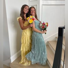 two girls in dresses standing next to each other holding flowers and smiling at the camera