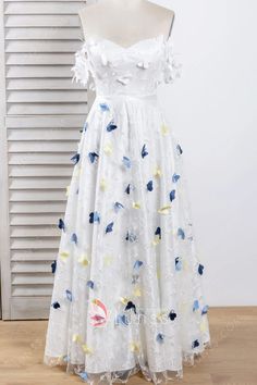 a white dress with blue and yellow flowers is on display in front of a window