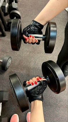 two pairs of feet with red nail polish and black gloves holding dumbbells in a gym